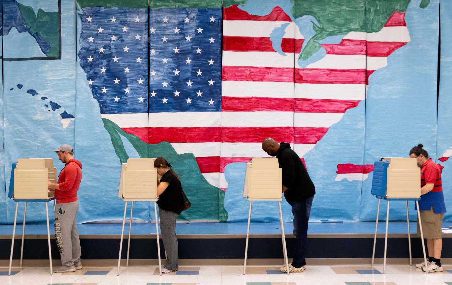Voters leaning over voting booths in front of an American flag mural.