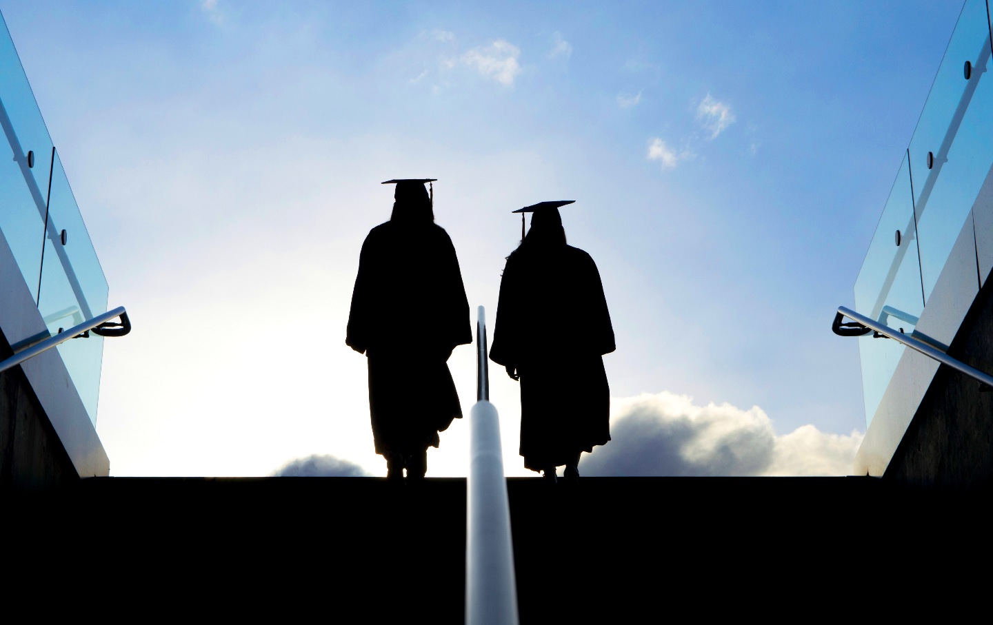 A shot of two college graduates as they make their way up a stairway.