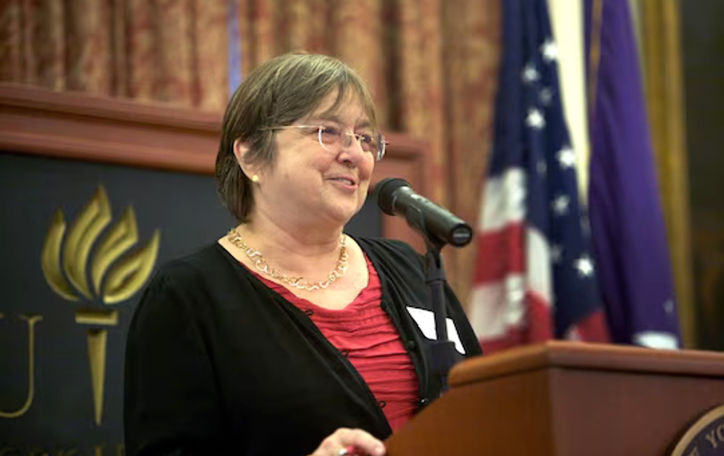 Holly Maguigan stands at a podium smiling, giving a speech.