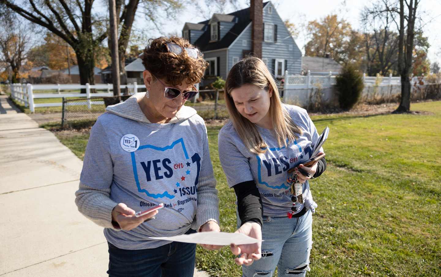 Two women look and discuss at turf maps on a suburban street in Ohio.