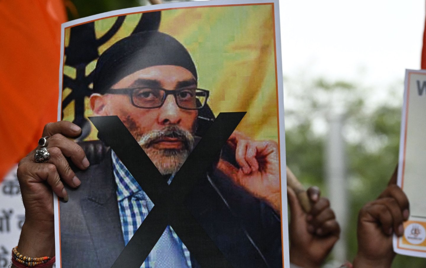 A hand holds a poster of Gurpatwant Singh Pannun's face with an X over it