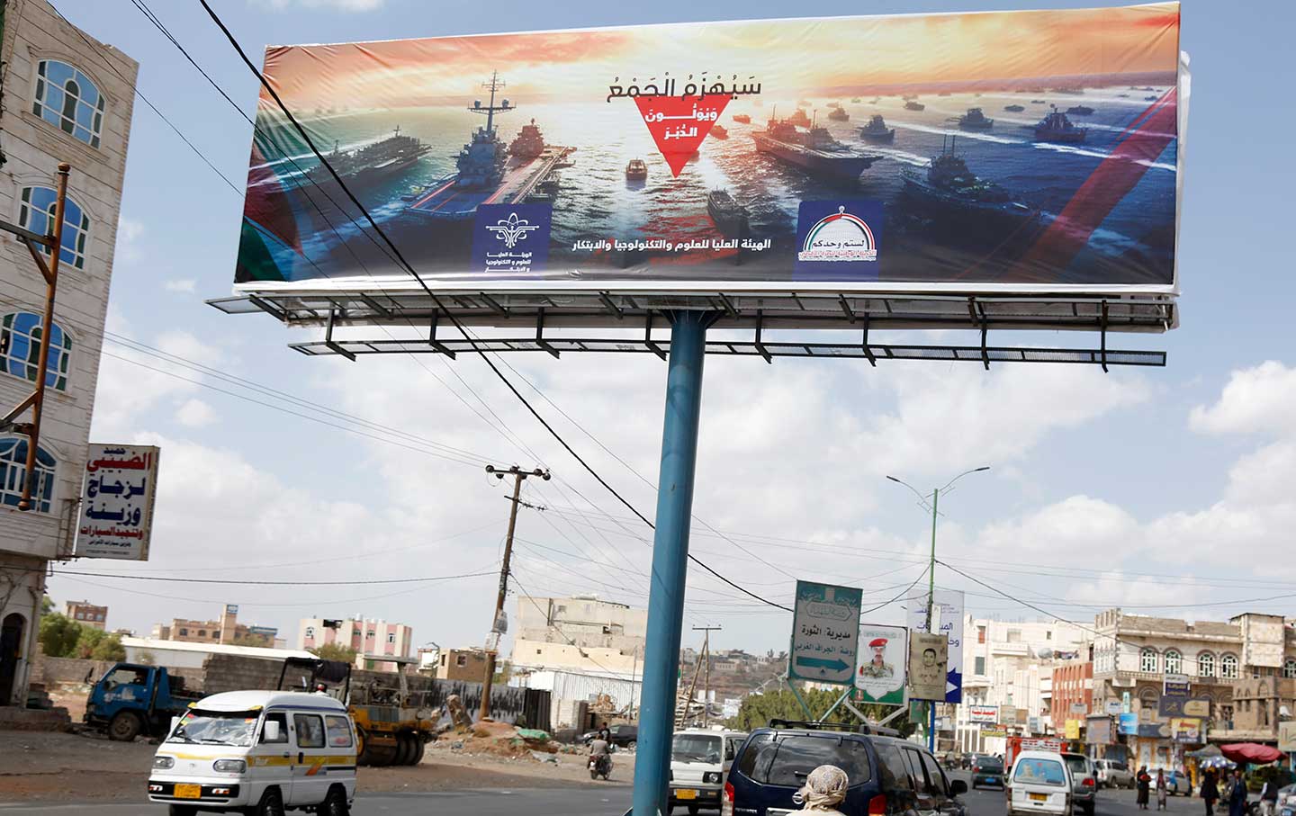 Yemenis drive past a large billboard with a picture depicting the navy destroyers of foreign countries including the US and UK, and the words “Navy coalition will be defeated” at a street on December 31, 2023 in Sana'a, Yemen.