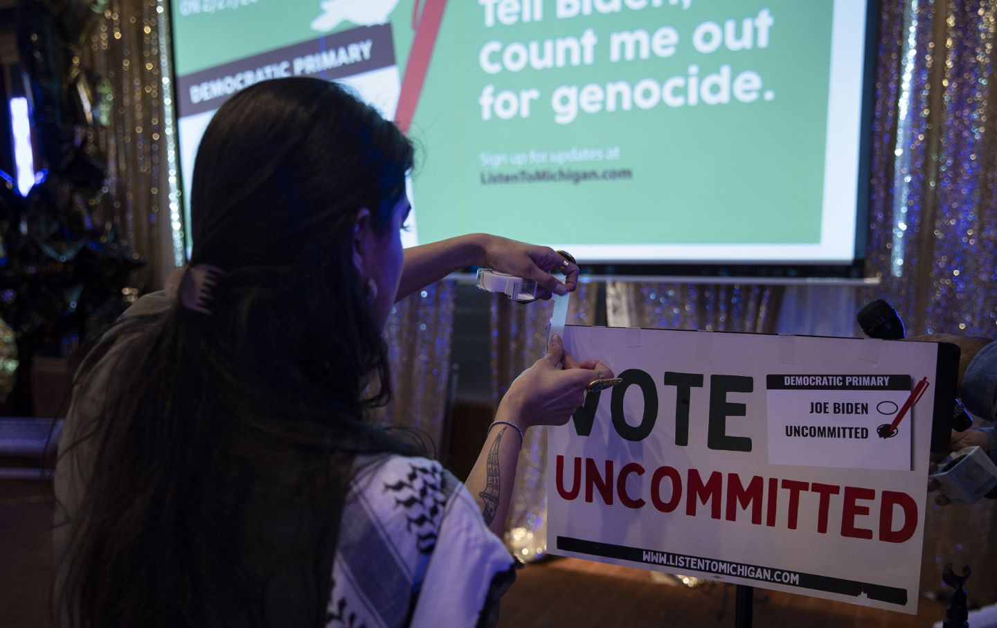 Natalia Katie places a sign on the podium before the beginning of the press conference for the group Listen to Michigan during its election-night watch party for the Michigan presidential primary election in Dearborn on February 27, 2024.