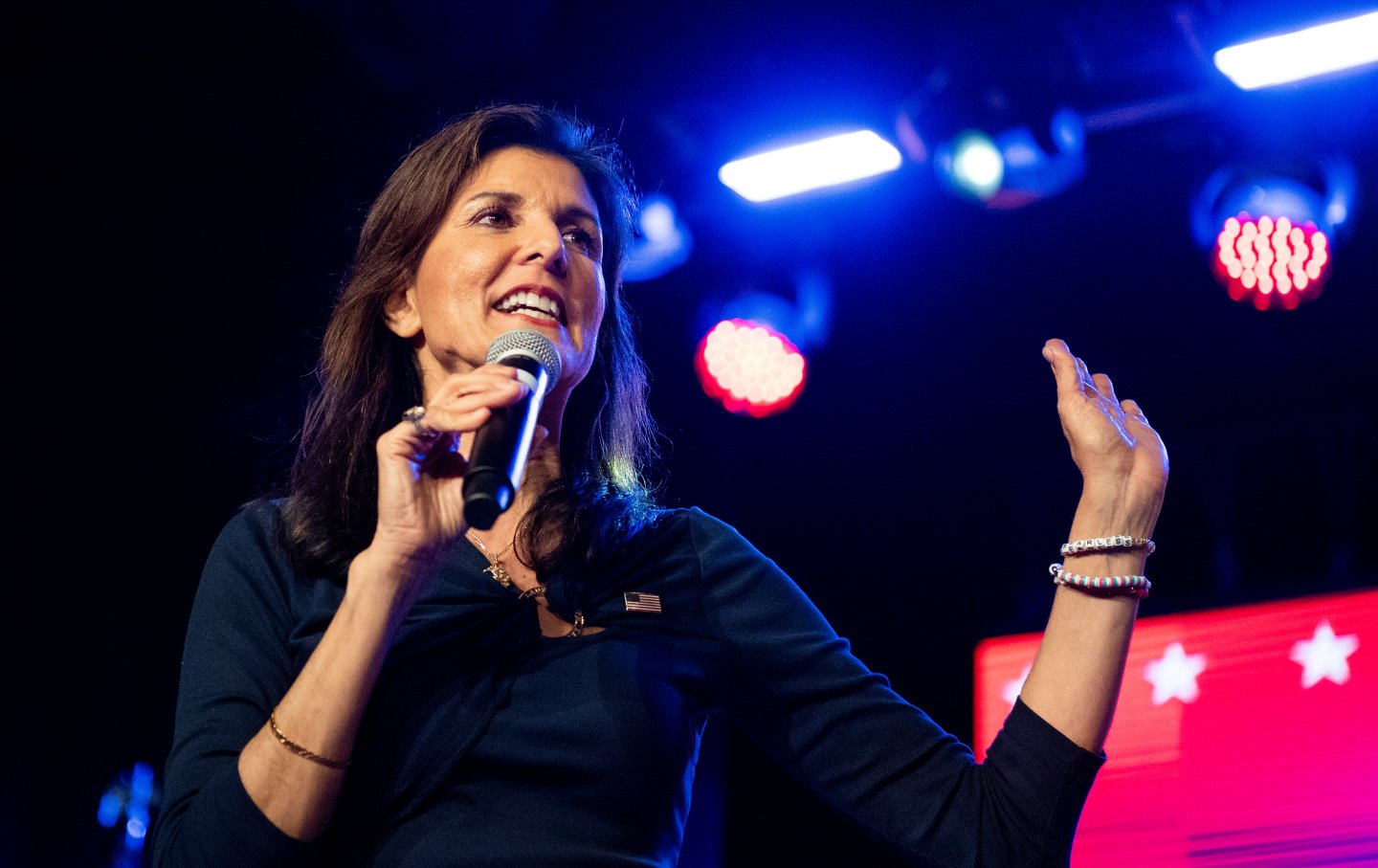 Nikki Haley holding a microphone on a rally stage.