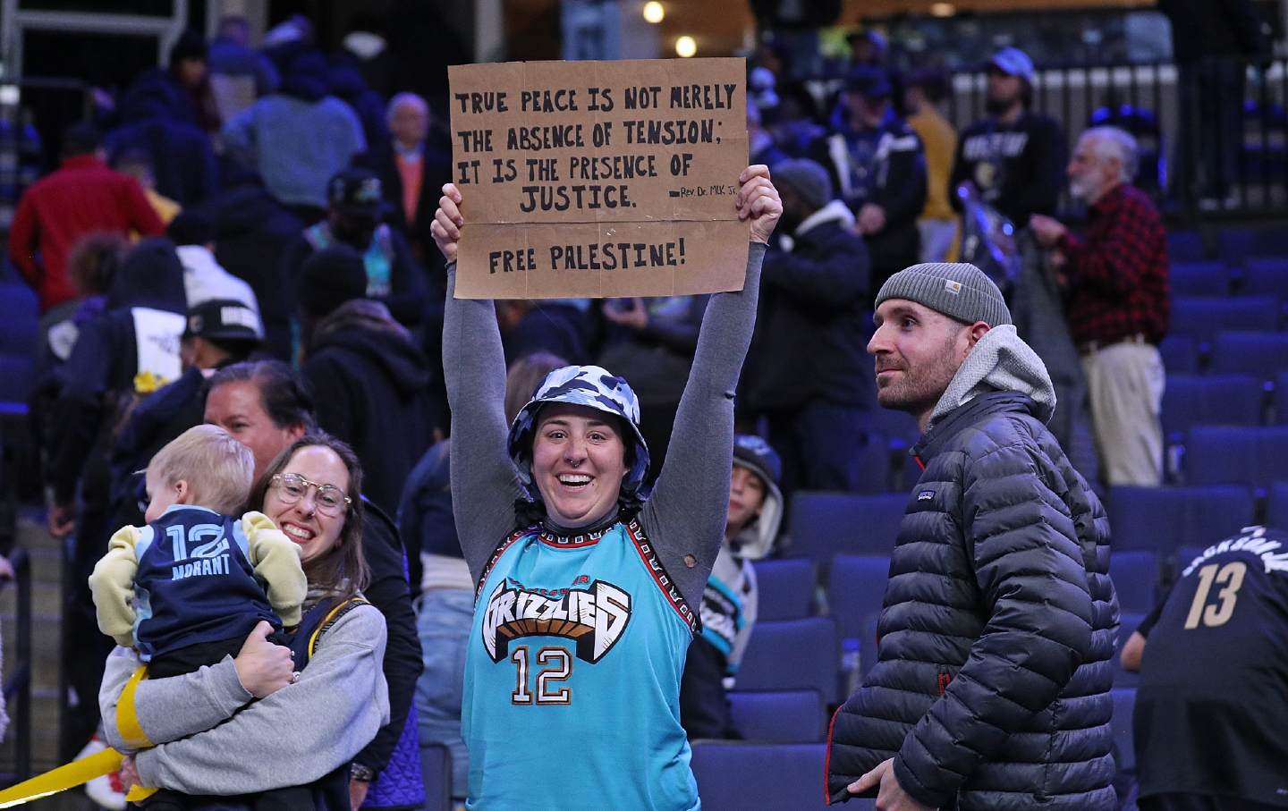 Woman in Grizzlies jersey holds up a pro-Palestine sign at a basketball game