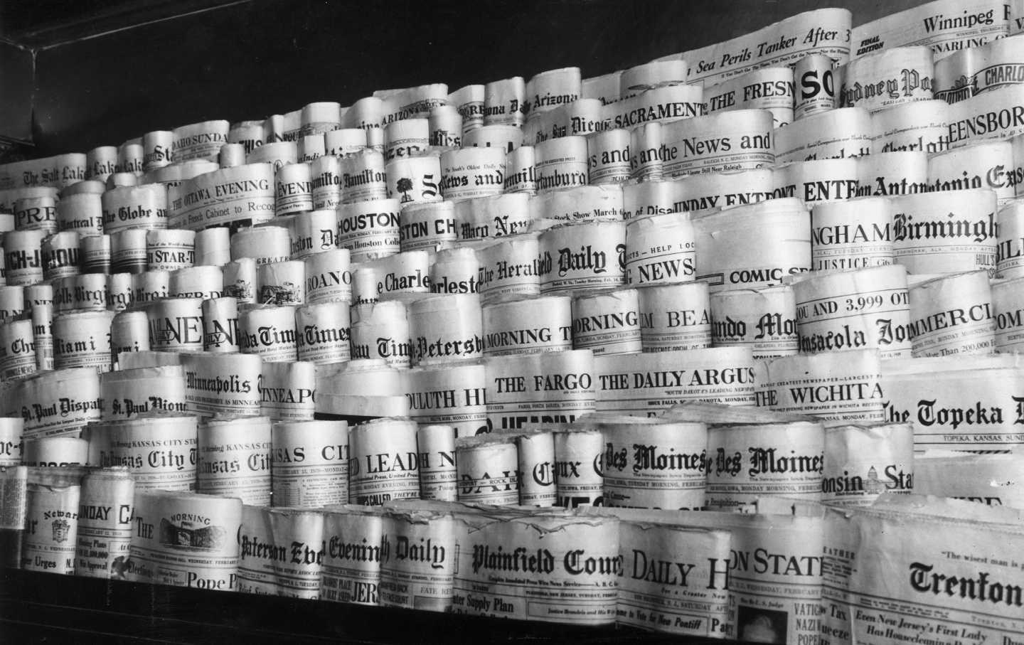 A display of dozens of local newspapers for sale on a newsstand in a black-and-white photo.