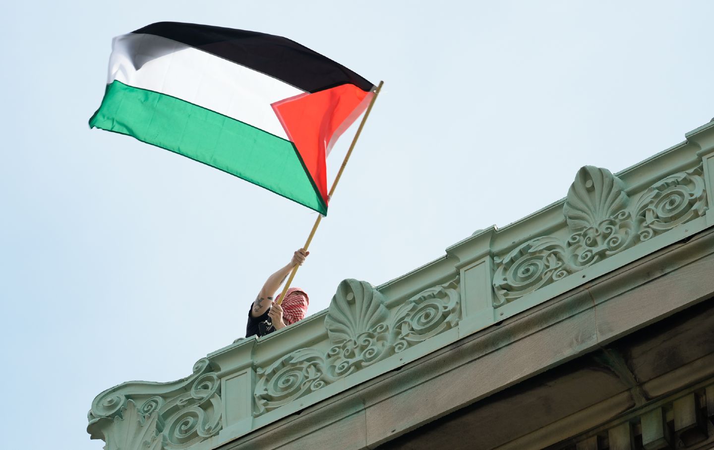 Protester in keffiyeh waves flag from roof