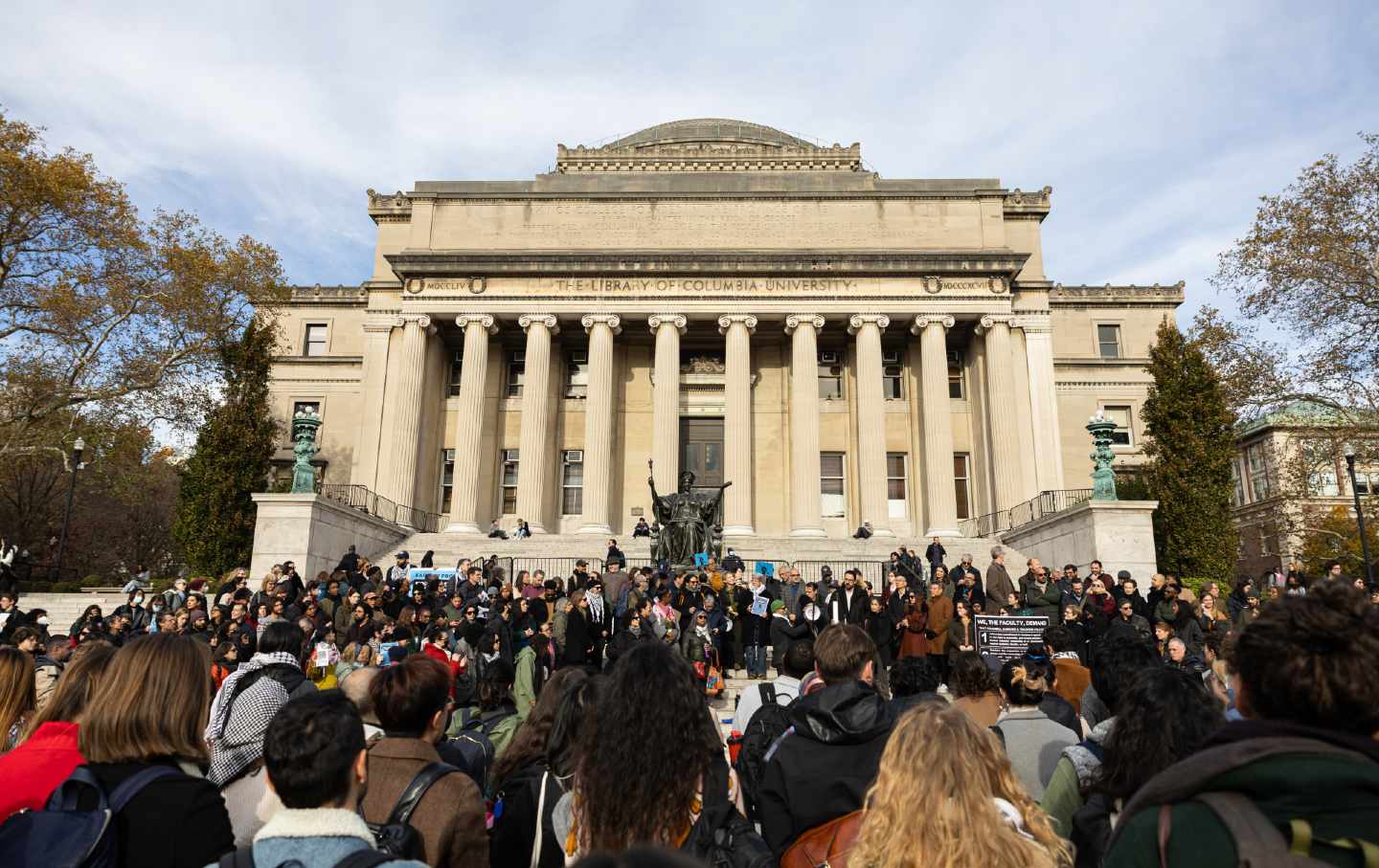 A crowd of students stands in front of a library at Columbia University protesting the university's decision to suspend two student groups