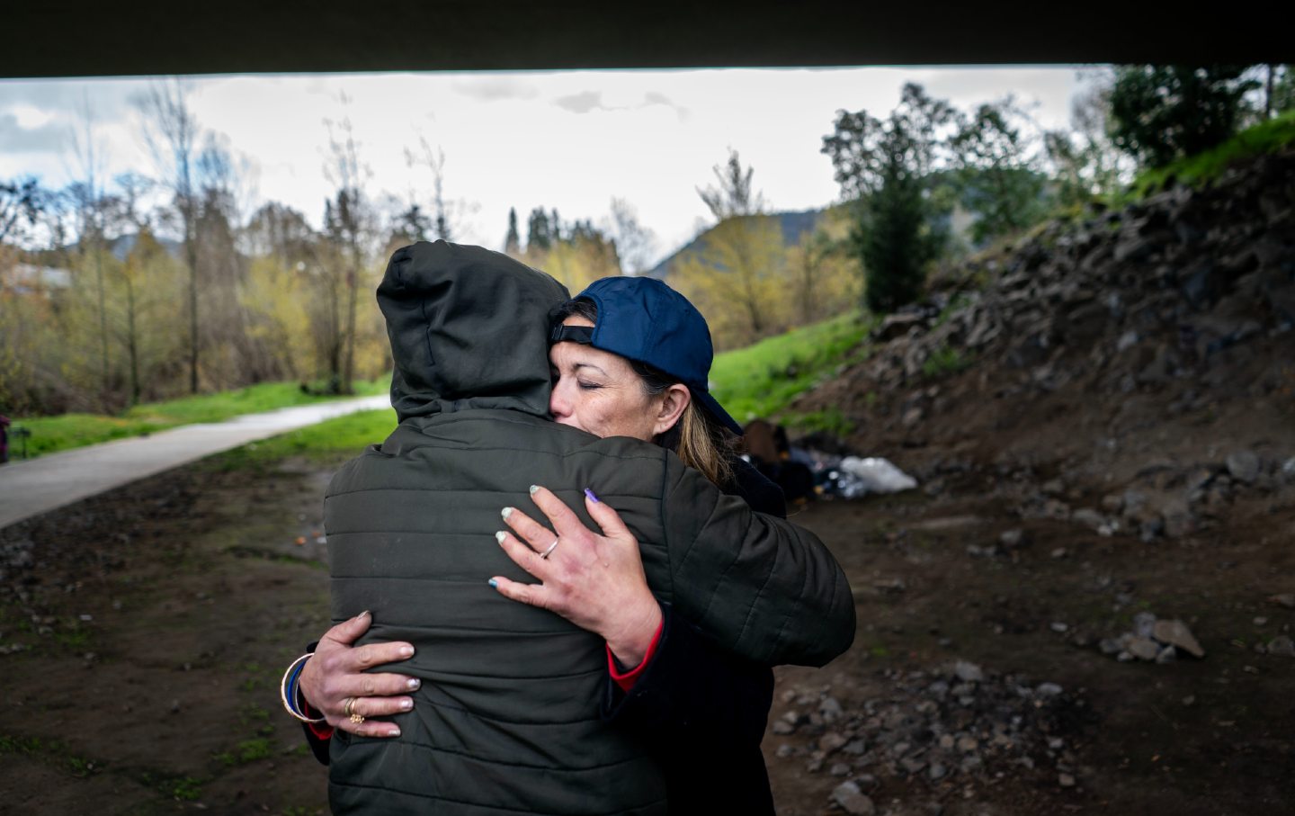 2024年3月28日木曜日、オレゴン州グランツパスのベイカーパークの橋の下で、住居のないキャンディ・ジーヴェルセンさん（右）が友人やホームレスコミュニティの仲間と抱き合う。