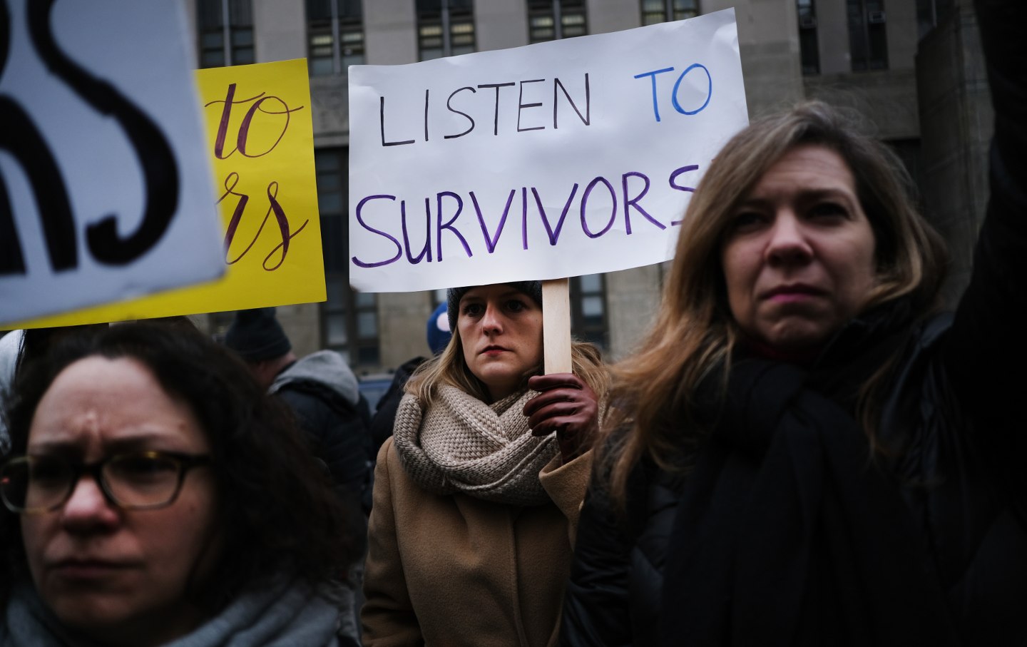 A photo of three women in a crowd at a protest of Harvey Weinstein, one holding a sign reading 