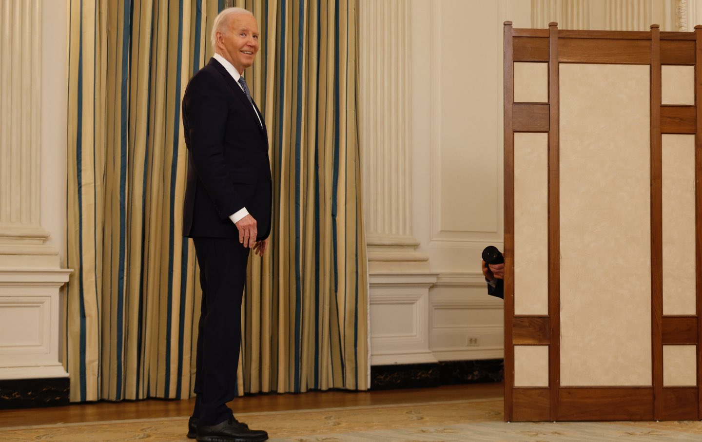 President Joe Biden looks back over his shoulder and smiles while leaving a press conference.