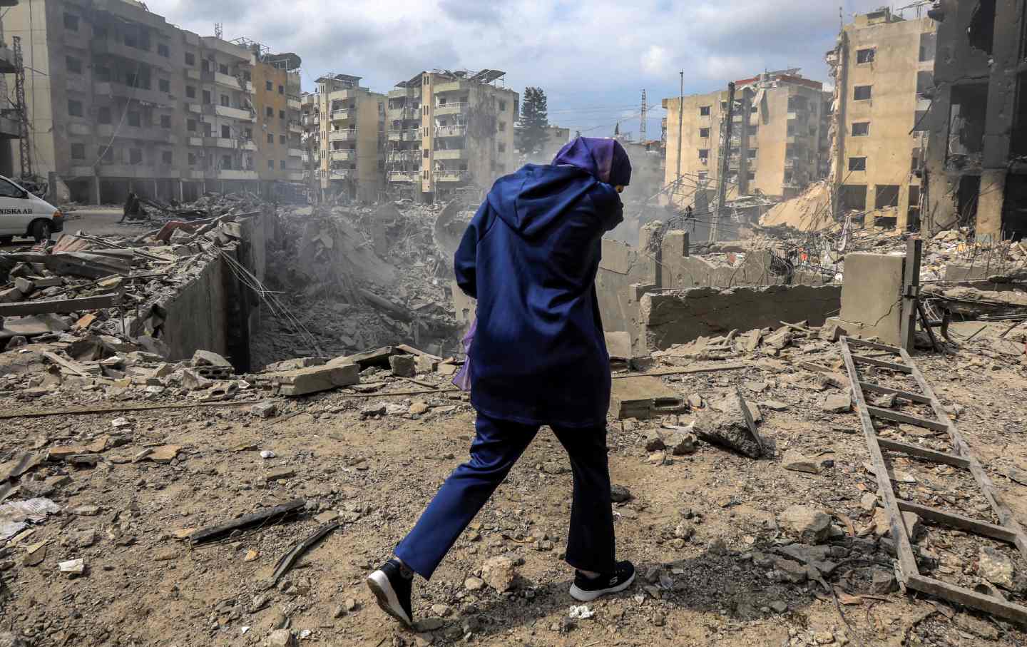 A woman walks past a crater where a collapsed building stood after an Israeli airstrike in a southern suburb of Beirut on October 7, 2024.