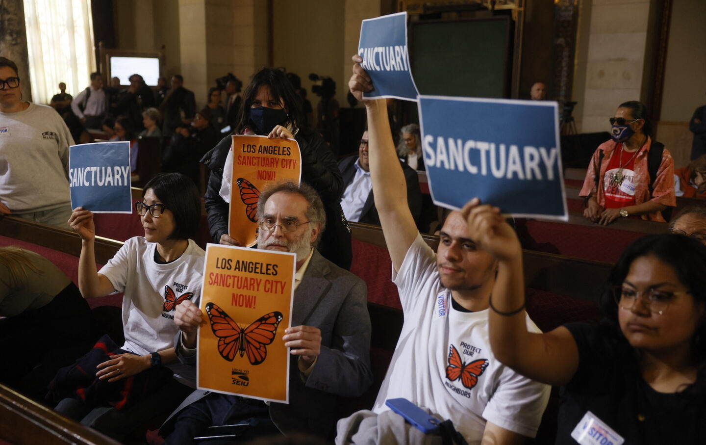 People in the audience hold up signs in support of immigrants as the Los Angeles City Council considers a