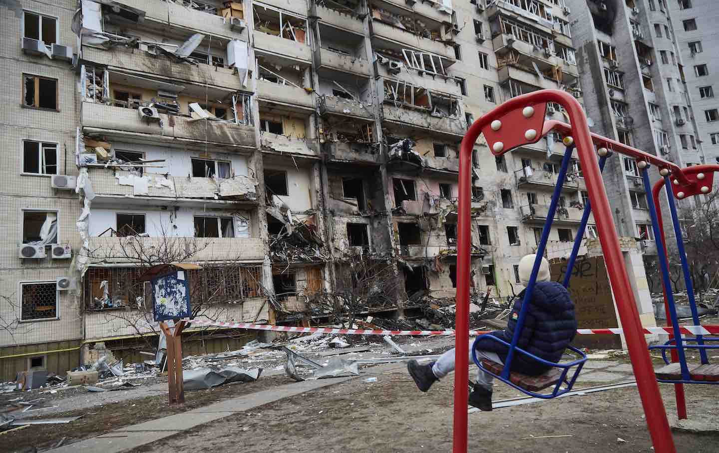 A child on a swing outside a residential building damaged by a missile in Kyiv, Ukraine, 2022.