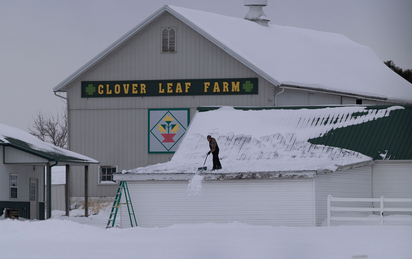 A farmer shovels snow from the roof of his building on December 09, 2025 near Belvidere, Illinois.