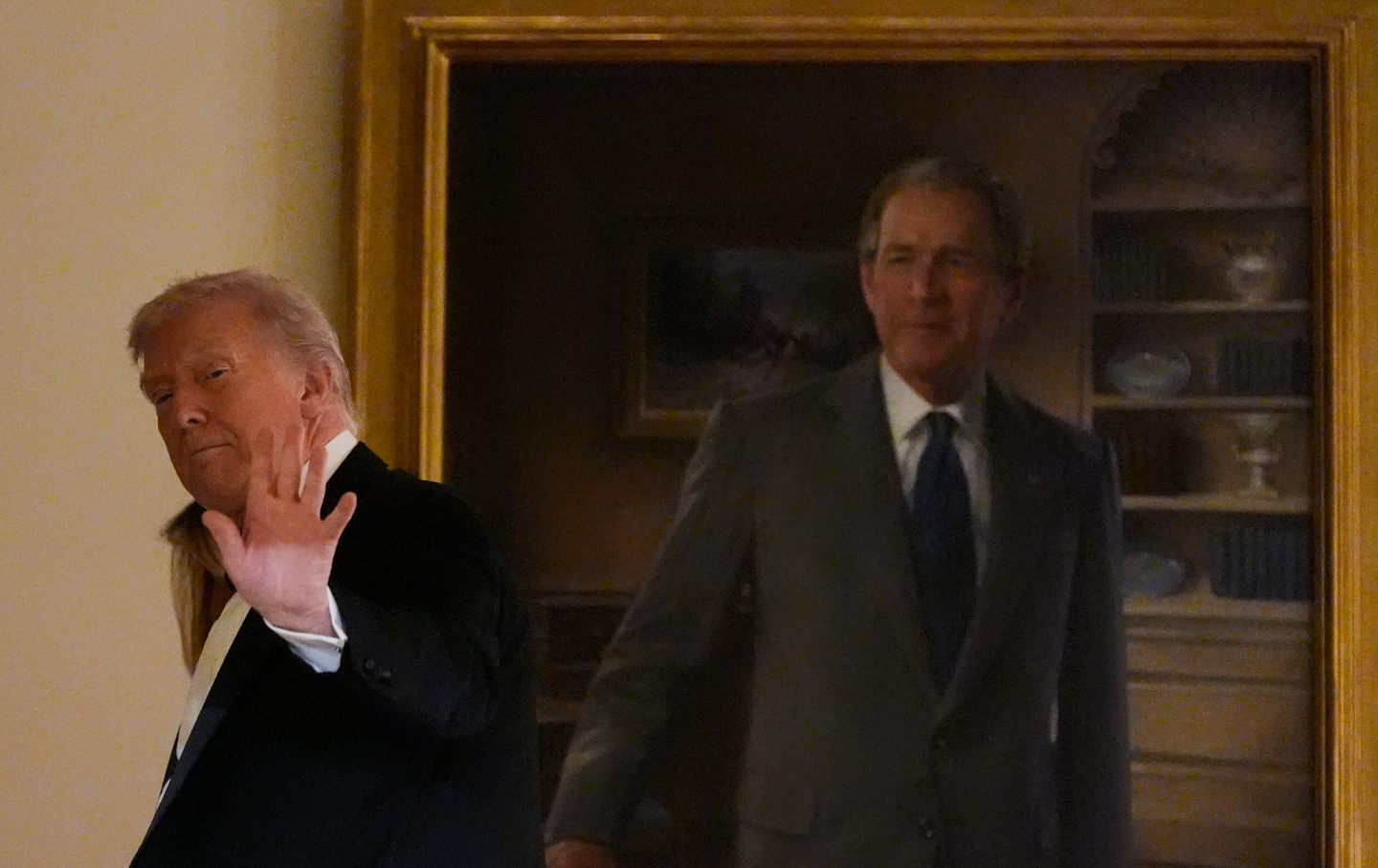 Donald Trump waves as he leaves passing a portrait of former President George W. Bush in the Grand Foyer of the White House during the Congressional Ball, Thursday, Dec. 11, 2025, in Washington.