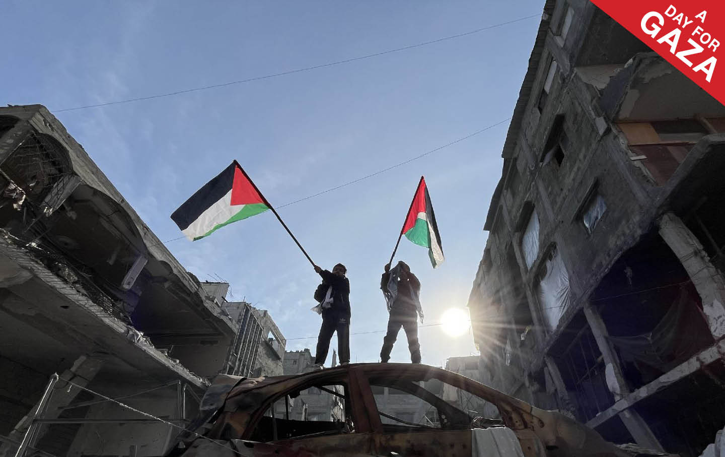 Two children are waving Palestinian flags on a wrecked car as displaced Palestinians start to return their houses past damaged houses in Jabalia and Beit Lahia regions