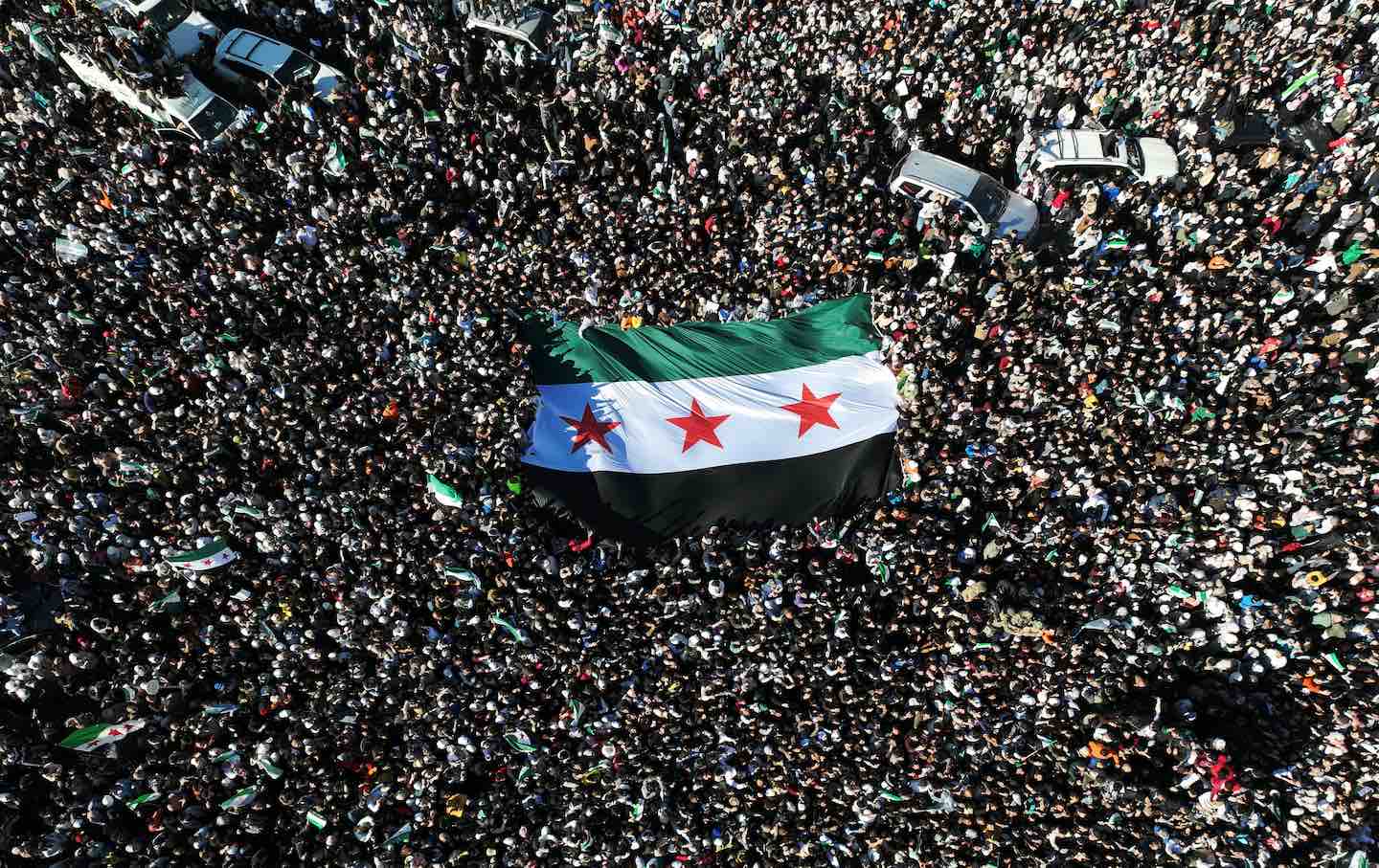 An aerial photo shows crowds of Syrians raising a giant independence-era flag, used by the opposition since the uprising began in 2011, as they celebrate the fall of Bashar al-Assad's rule earlier this week at the central Umayyad Square in Damascus on 2024.