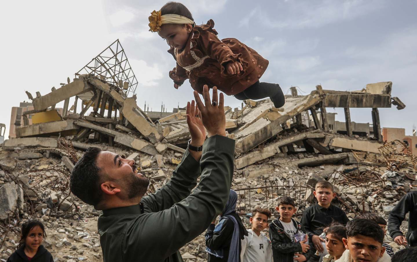 A man tosses a baby into the air as Palestinian children receive Eid treats distributed volunteers of a charity organization on the second day of Eid al-Fitr amid rubbles in Khan Yunis, Gaza on March 21, 2026.