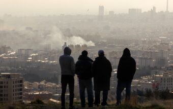 Men watch from a hillside as a plume of smoke rises after an explosion on March 2, 2026, in Tehran, Iran.