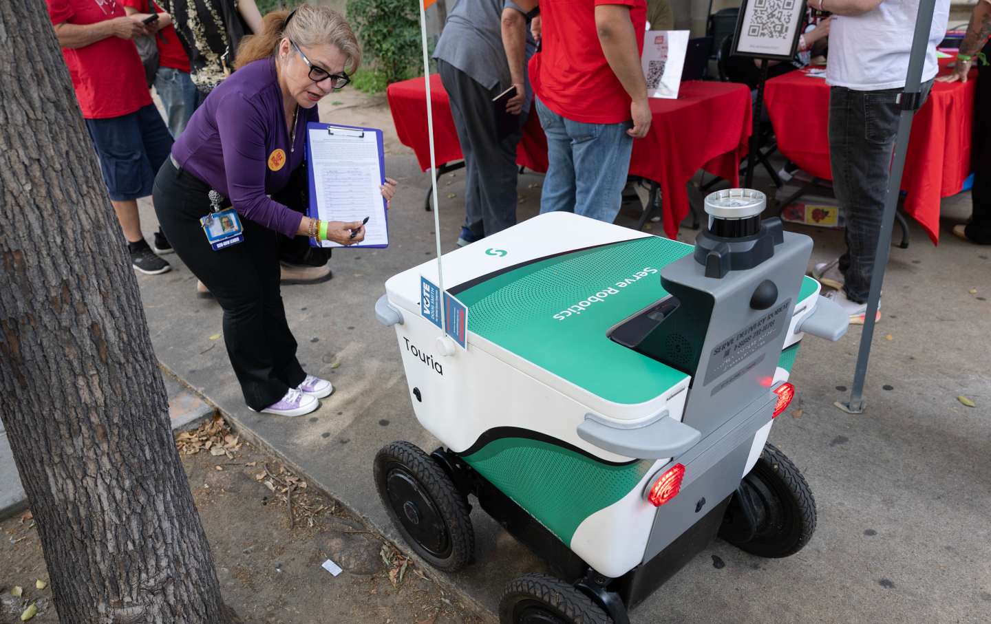 Josephine Rios of Service Employees International Union–United Healthcare Workers West, asks a delivery robot if it wants to sign a petition to tax billionaires, in Koreatown, Los Angeles, on March 21, 2026.