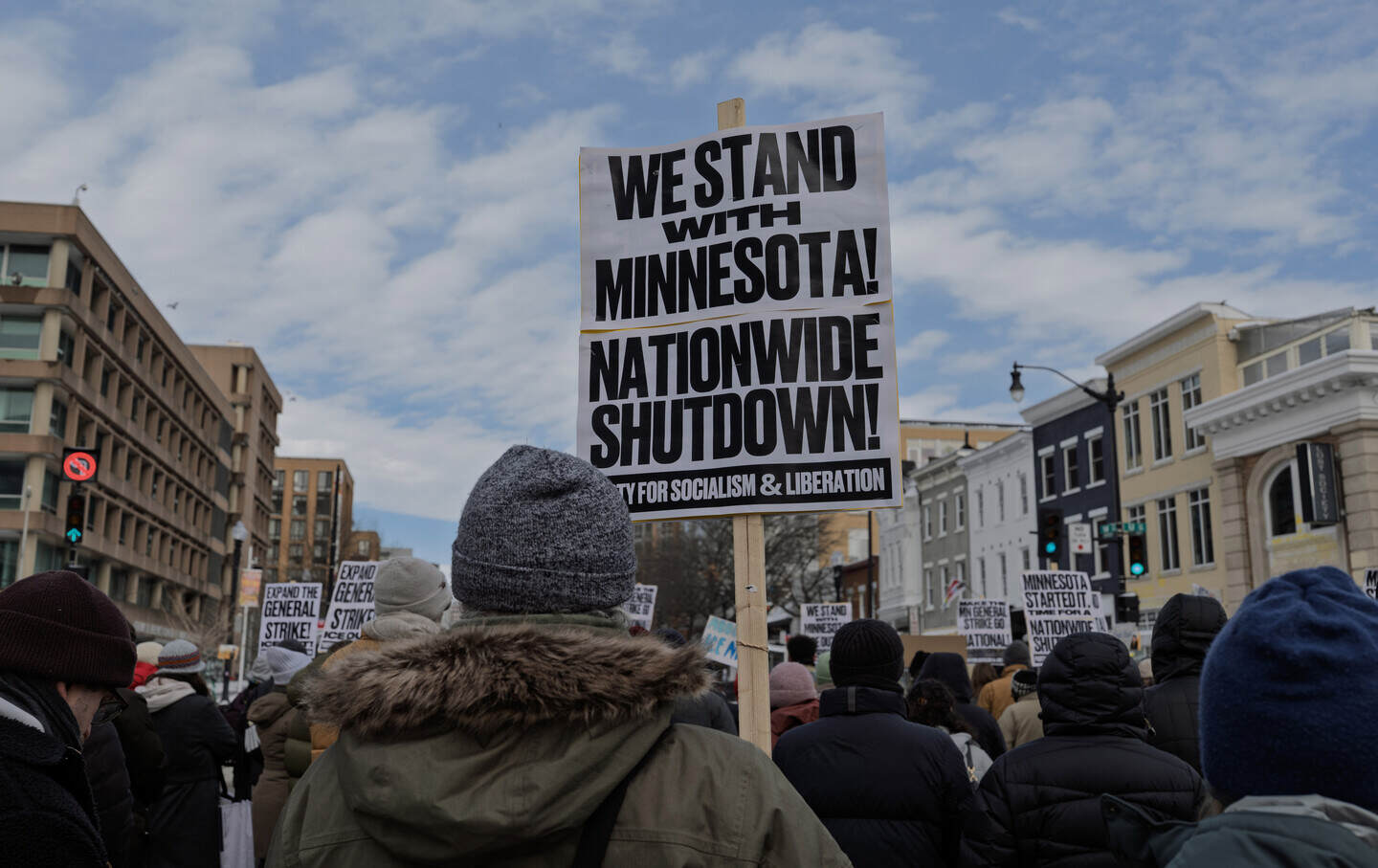 A demonstrator holds an anti-ICE sign that reads “We Stand with Minnesota, Nationwide Shutdown” while joining a protest.