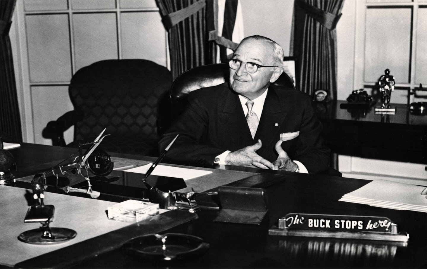 American President Harry S. Truman seated in White House library, with “The Buck Stops Here” on a placard in foreground, circa 1950.