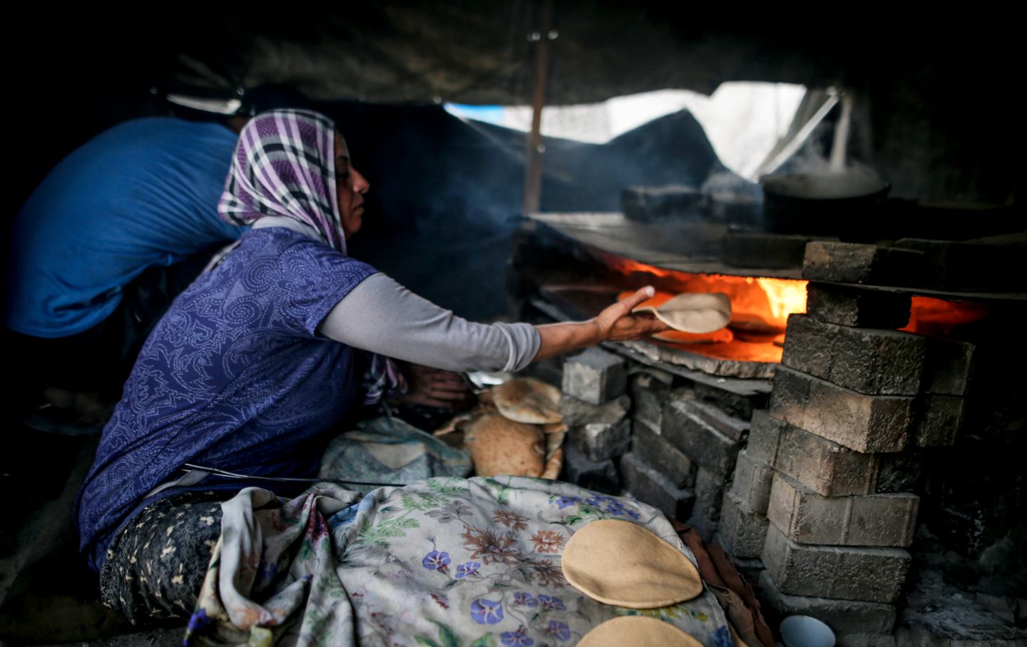 A displaced Palestinian woman bakes bread inside a damaged building at the Islamic University in Gaza City on April 18, 2026.