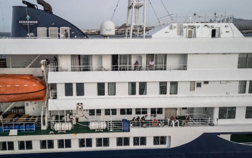 Passengers watch as unseen health personnel assists patients onto a boat from the cruise ship MV Hondius, while stationary off the port of Praia, the capital of Cape Verde, on May 6, 2026. Evacuations were taking place because of a deadly outbreak of hantavirus.