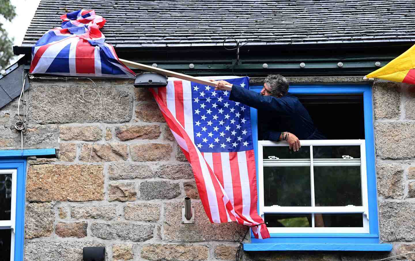 The owner of The Cornish Arms gastropub adjusts the Union Flag alongside the American flag on the exterior of the pub in St. Ives, Cornwall on June 10, 2021.