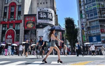 A woman carries an umbrella to shelter from the sun as pedestrians cross a street in the Kabukicho entertainment area of Shinjuku in central Tokyo on July 29, 2025.