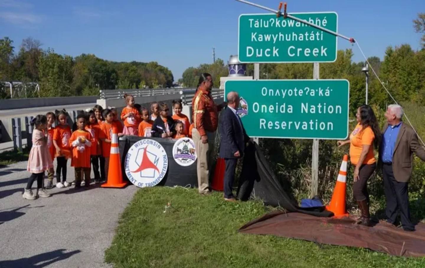 Representatives from the Oneida Nation, the Wisconsin Department of Transportation, and the Federal Highway Administration unveil new dual-language signs in Oneida, Wisconsin, on September 30, 2022.