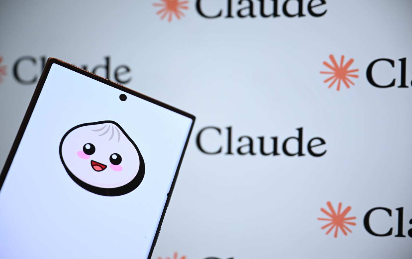A phone displaying the logo for Anthropic's Javascript property, Bun, brandished before a display of logos for the company's chatbot, Claude.