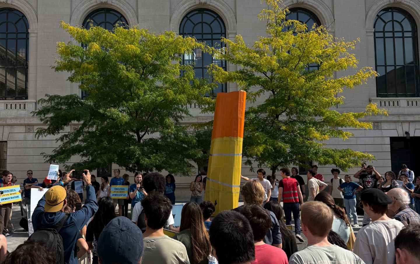 A crowd gathered around a 12-foot cardboard version of Claes Oldenburg’s lipstick sculpture to protest their university and government.